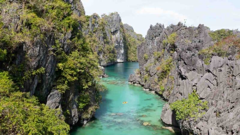 Yellow Kayak paddling through Big Lagoon on Miniloc Island in El Nido with Aqua colored water and tall limestone rock cliffs surrounding