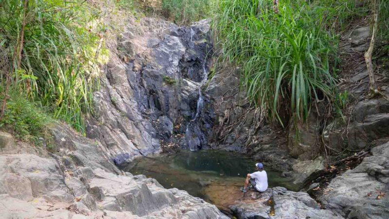 Man sitting infront of a waterfall in El Nido called Nagkalit Kalit