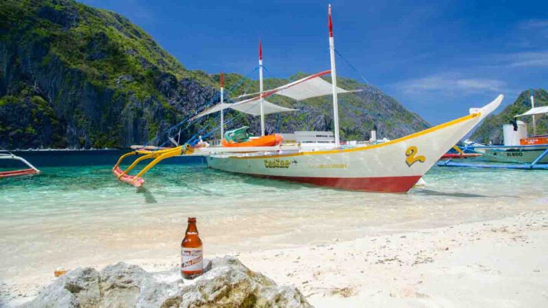 Local drink placed on a rock in front of a traditional Filipino boat - El Nido Palawan Philippines