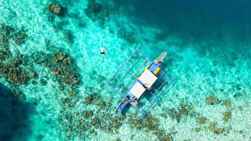 man swimming in the Twin Lagoon of Coron - Turquoise waters and traditional Filipino boat