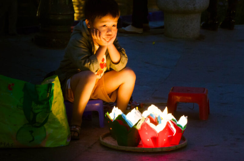 A young vietnamese boy sits at the river bank selling lanterns for the Hoi an full moon lantern festival
