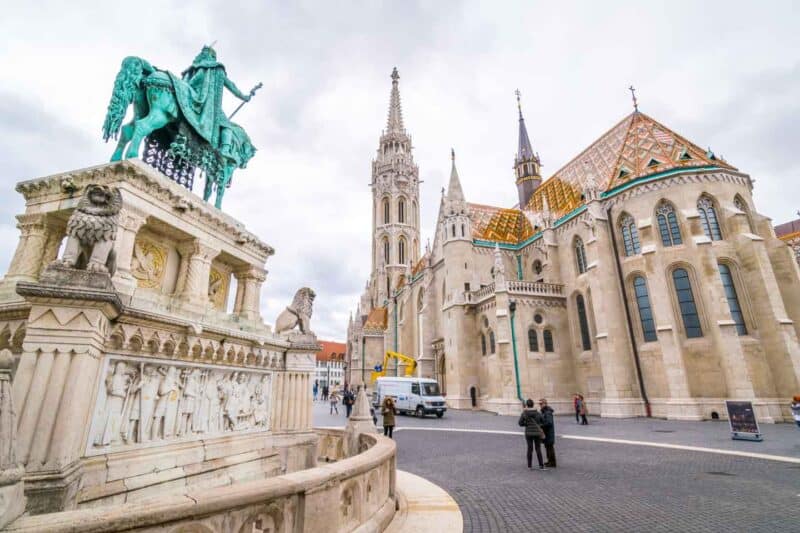 A green copper statue in front of the Matthias Church in Budapest