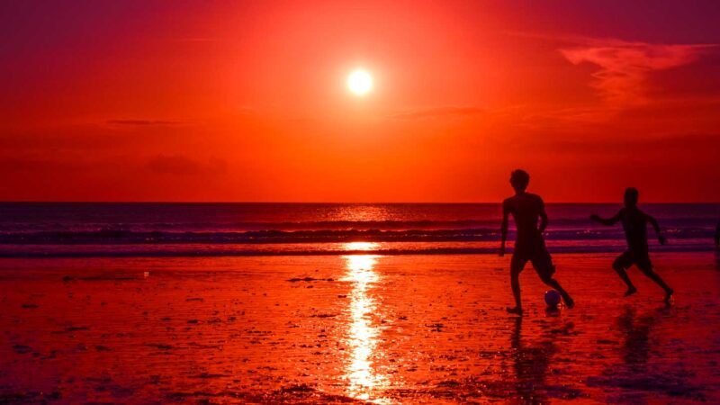 Boys playing football on the beach as the sunsets