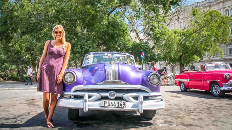 Girl leaning on purple classic car in Cuba