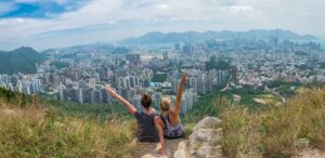 two women sitting on the edge of a cliff over looking hong kong from Lion rock peak