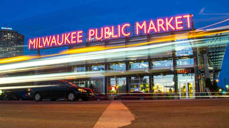 View of the exterior of the Milwaukee Public Market at night with traffic passing by - Top Milwaukee Attractions