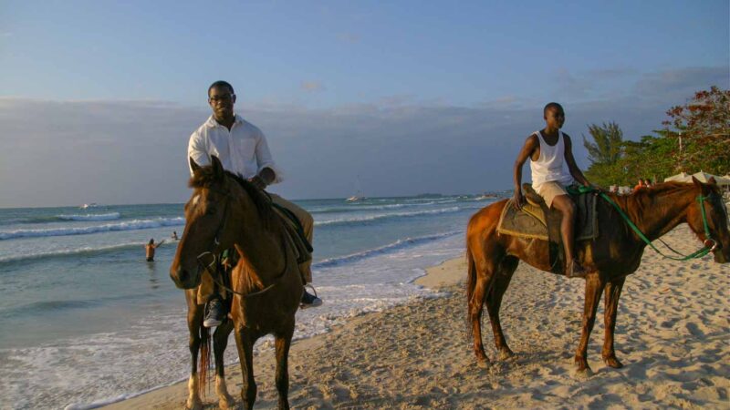 Two men riding horses on the beach in Negril Jamaica