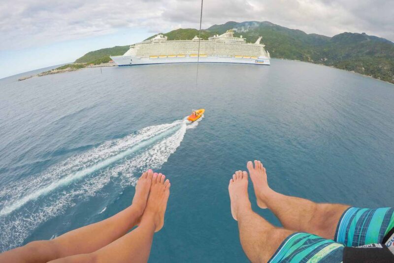 A couple parasailing in the Labadee port in front of the Oasis of the Seas Royal Caribbean ship