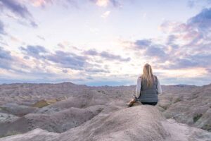 woman sitting on a ledge during sunset in badlands national park on a south dakota road trip