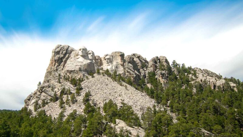 Long exposure photo of mt rushmore with streaky clouds and blue sky