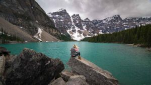 Woman sitting in front of Moraine LAke on the drive to Alaska