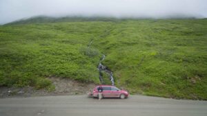 Minivan campervan parked in front of a green hill with a waterfall in Alaska