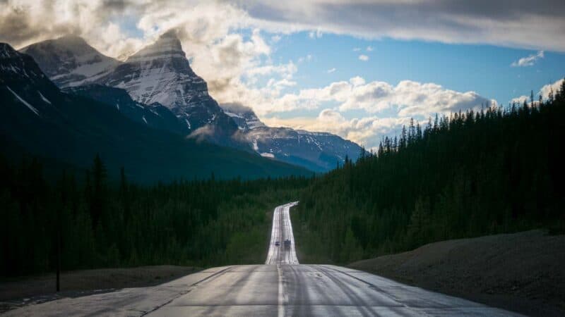 long section of road with a steep down hill surrounded by mountains on the drive to Alaska