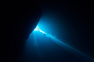 Divers swimming in a light beam in El Pit Cenote