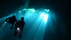 Two divers with flash lights descend in El Pit Cenote with light beams