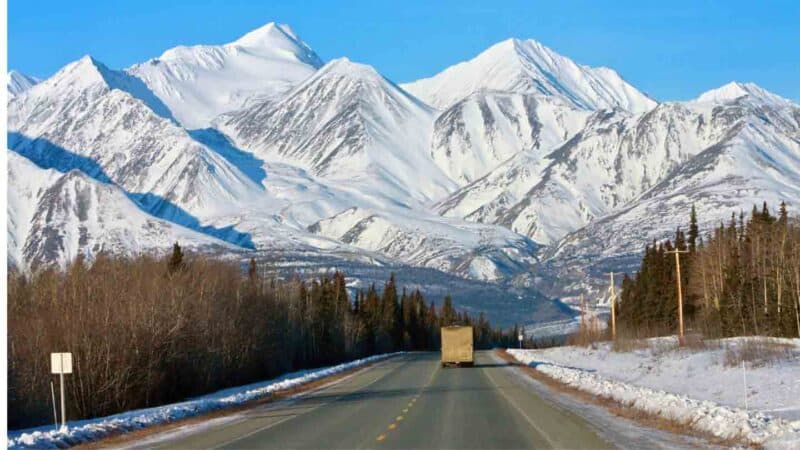 Alcan Highway, the road to Alaska, with snow covered mountains in the background