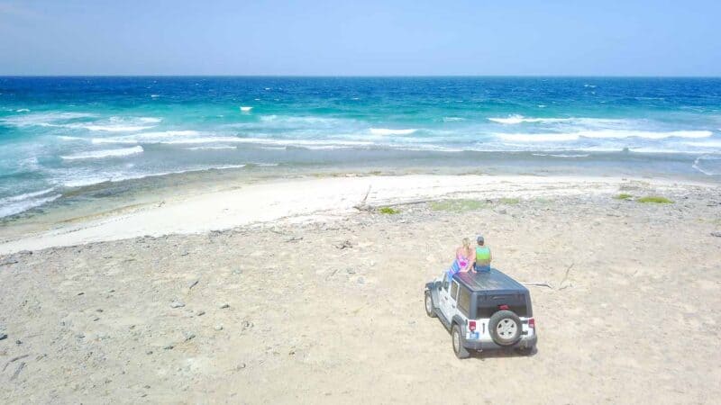 a couple sitting on the roof of a rental jeep in Aruba during a honeymoon