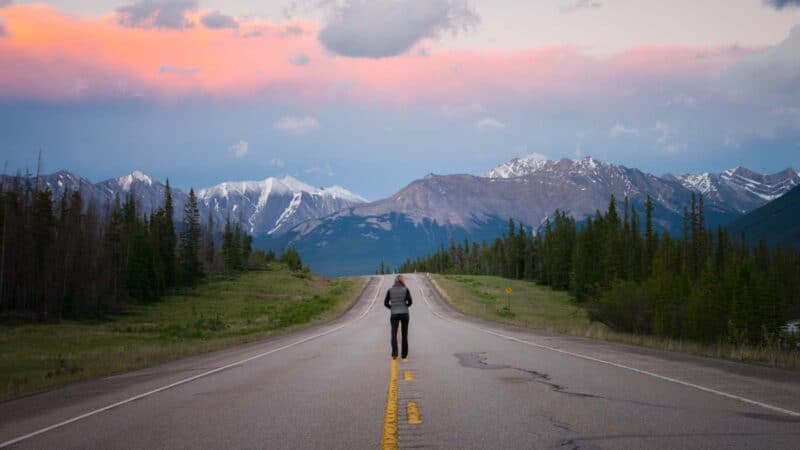 Woman standing in the middle of the Alcan Highway on a road trip to Alaska