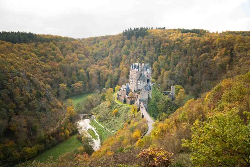 Distant Viewpoint view of Eltz Castle surrounded by trees and river in the fall