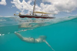 Woman swimming in front of a sail boat in anfuilla captured by a GoPro Dome photo hal under and half over the waterline
