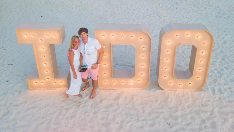 couple standing in front of an "I Do" light up sign on an Aruba Honeymoon on the beach