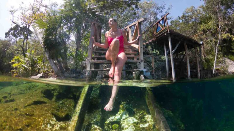 woman with her feet in the clear waters of Cenote Jardin del Eden near Palay del Carmen and Tulum Mexico in an over/under photo via a gopro dome
