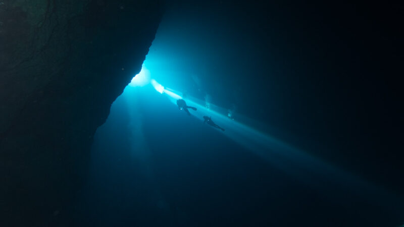 two diver swim through a light beam in the El Pit Cenote near Tulum - Best cenotes in Tulum 