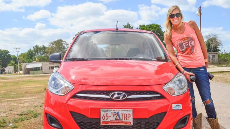 woman standing next to a rental car in Cancun after picking it up from the airport