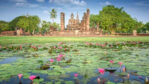 view looking over a lilly pad covered lagoon on to a Buddha statue in the Acient Thai city of Sukhothai - Top Attractions in Thailand