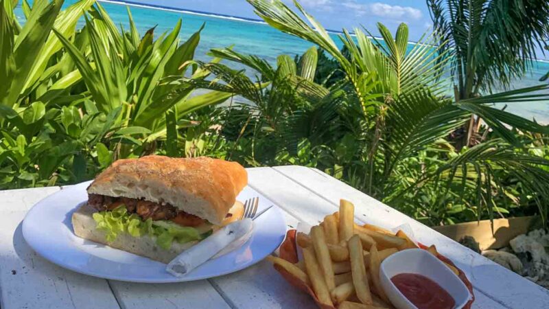 Chicken Sandwich & Chips on a picnic table with the ocean in the background at Charlie's Cafe restaurant in the Cook Islands