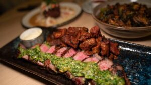 A plate of cut steak with a green chimichurri sauce served at one of Milwaukees top restaurants - Eldr and Rime
