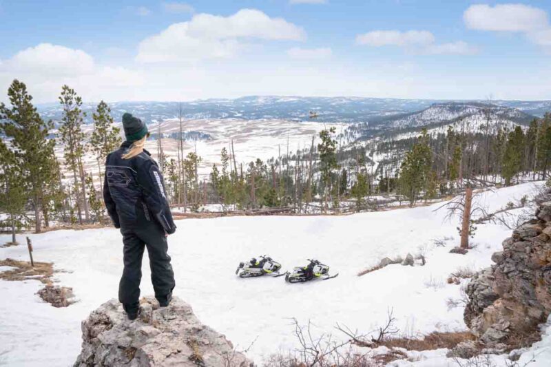 Woman standing on top of the Flag Mountain Overlook while snowmobiling in the Black Hills of South Dakota