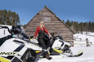 Woman standing with a snowmobile in front of an old wooden building in the Black Hills