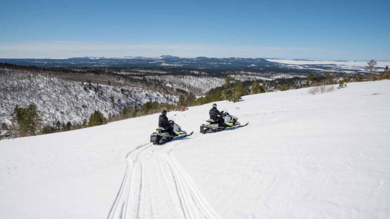 Two people riding snowmobiles on Trail #2 in the Blackhills at the Cement Ridge Overlook