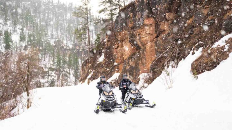 couple riding snowmobiles in the Black hills with snow falling