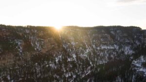 Drone photo of the sunrise before a snowmobile ride over spearfish canyon - yellow sunlight with snow covered pines and steep hills
