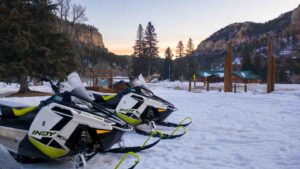 two Polaris Adventures Snowmobiles parked at the Spearfish Canyon Lodge at Sunrise - Orange and Blue skies with white and yellow sled in the foreground