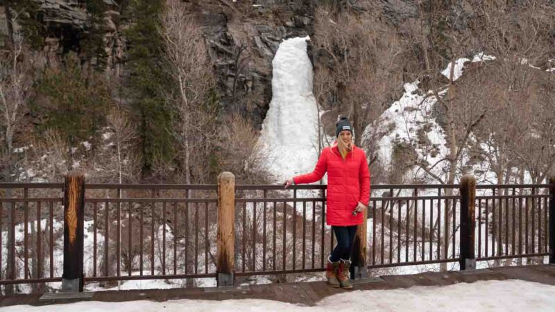 woman in a red jacket standing in front of Bridal Veil Falls in Spearfish Canyon, SD - Frozen waterfall - top things to see in the winter in the Black Hills, SD