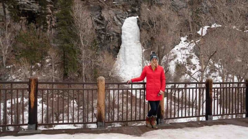 woman in a red jacket standing in front of Bridal Veil Falls in Spearfish Canyon, SD - Frozen waterfall - top things to see in the winter in the Black Hills, SD