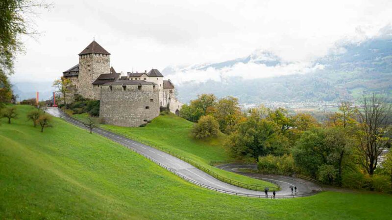 Camino pavimentado que conduce al palacio real del castillo de Vaduz - Cosas que hacer en Liechtenstein con montañas al fondo
