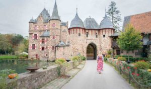 woman in a red dress walking into the historical Burg Satzvey in Germany