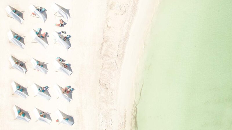 Foto de drones de clubes de playa en Isla Holbox México - Pequeñas carpas blancas en la playa con agua de color aqua