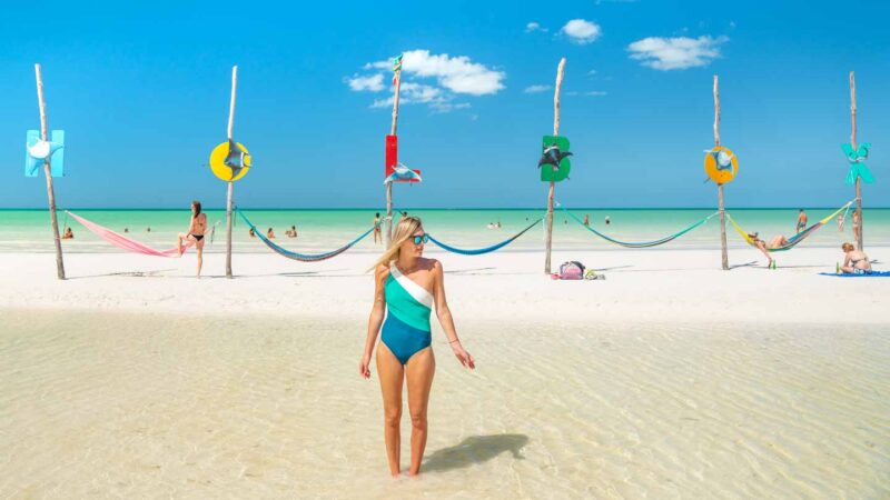 woman standing in front of the famous hammocks on the beach on Holbox Island - with signs spelling out "HOLBOX"