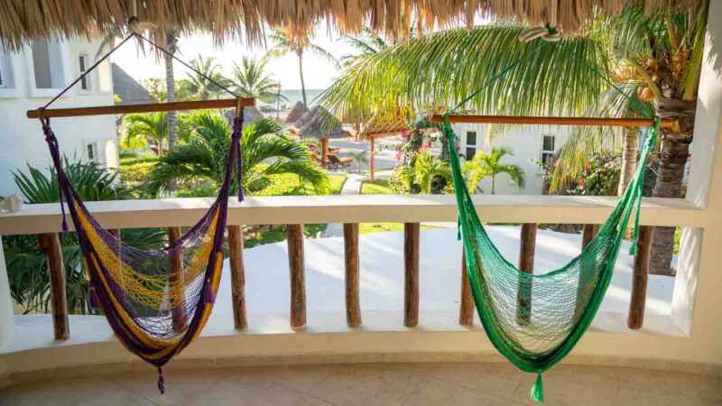 two hammocks hang from a ceiling with a thatched palm roof - Where to stay Isla Holbox Island Mexico
