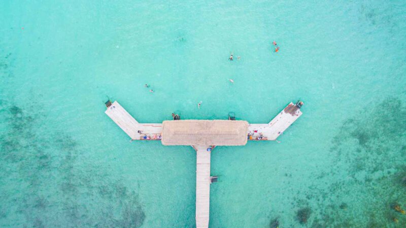 Aerial view of Thatched hut on the end of a dock in Laguna Bacalar Mexico - Aqua colored water and tan palm thatching