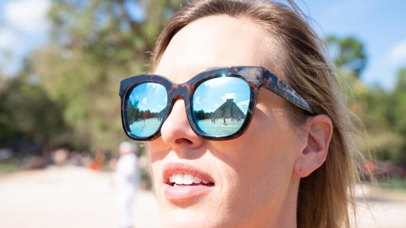 Woman wearing sunglasses with the reflection of Chichén Itzá in the lenses