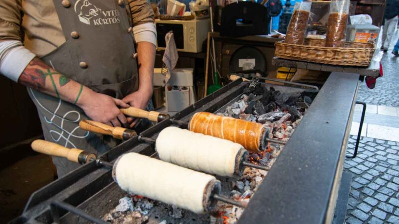 Man selling Chimney Cakes at a Budapest Christmas Market - Circular Dough roasted on a tube over hot coals