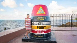 woman in a striped dress standing next to the "Southernmost Point" Marker Buoy - top tourist attractions while driving to key west florida