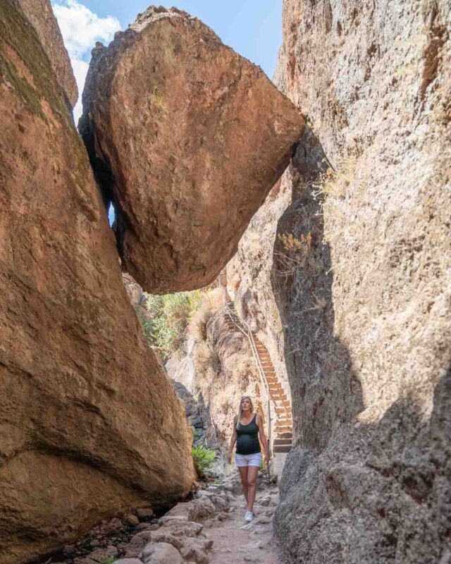 Woman standing under hanging rock inside of Pinnacles National Park - Cali Road Trip Ideas
