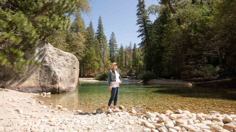 Woman standing in front of Muir Rock with clear water in the background - Kings Canyon National Park Road Trip
